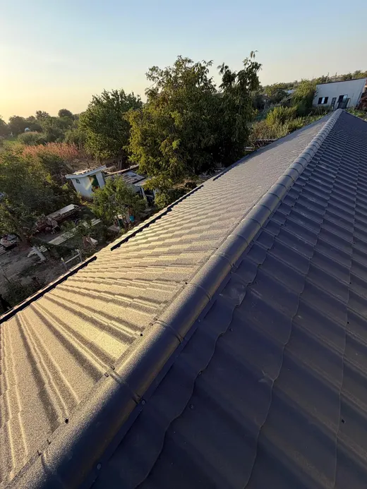 Pantă de tablă metalică antracit la apus, cu umbra lucrătorului pe acoperiș