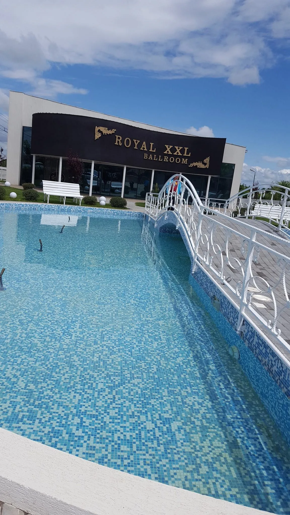 Piscina albastră cu podeț alb și clădirea în fundal